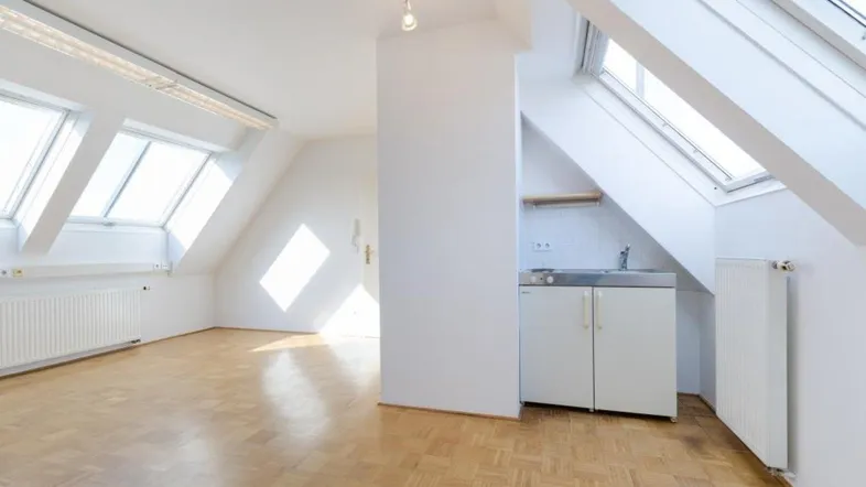 Helles Dachgeschosszimmer mit Parkettboden, schrägen Wänden, Dachfenstern und einer kleinen Küchenzeile.