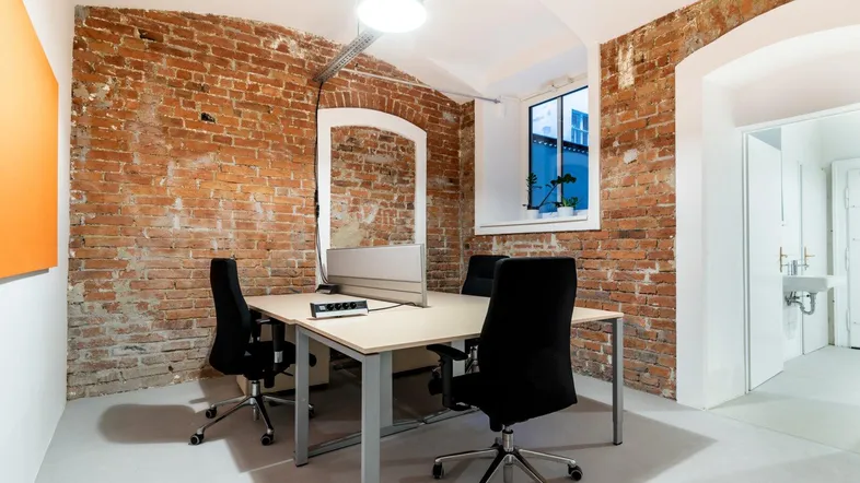 Modernes Büro mit freigelegten Ziegelwänden, einem Schreibtisch und einem Fenster, das Tageslicht hereinlässt.