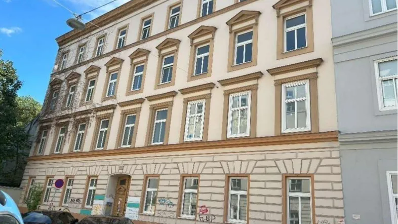 Historische Fassade eines Altbaus mit vielen Fenstern und dekorativen Elementen an einer Stadtstraße.