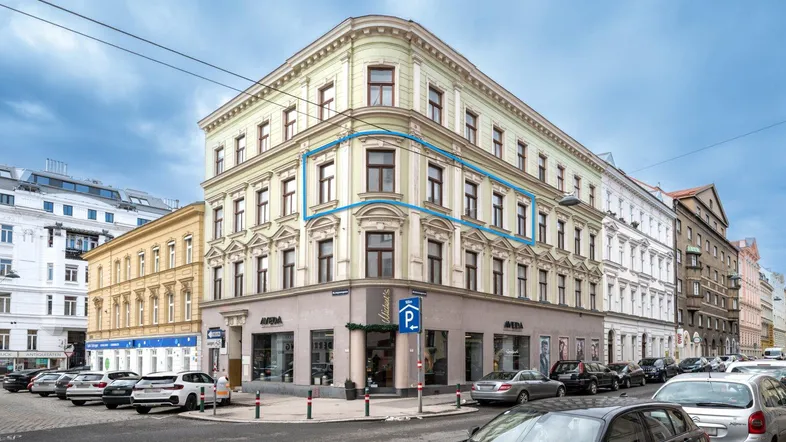 Historisches Eckgebäude mit klassischer Architektur und Geschäften im Erdgeschoss an einer belebten Straße.
