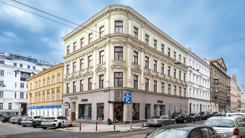 Historisches Eckgebäude mit klassischer Fassade und Geschäften im Erdgeschoss an einer belebten Straße.