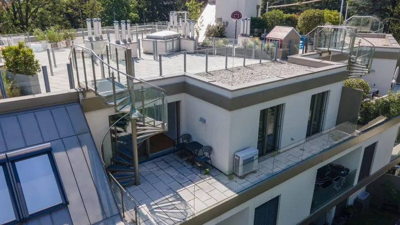 Dachterrasse mit Wendeltreppe und Glasgeländer, umgeben von Bäumen und weiteren Terrassen.