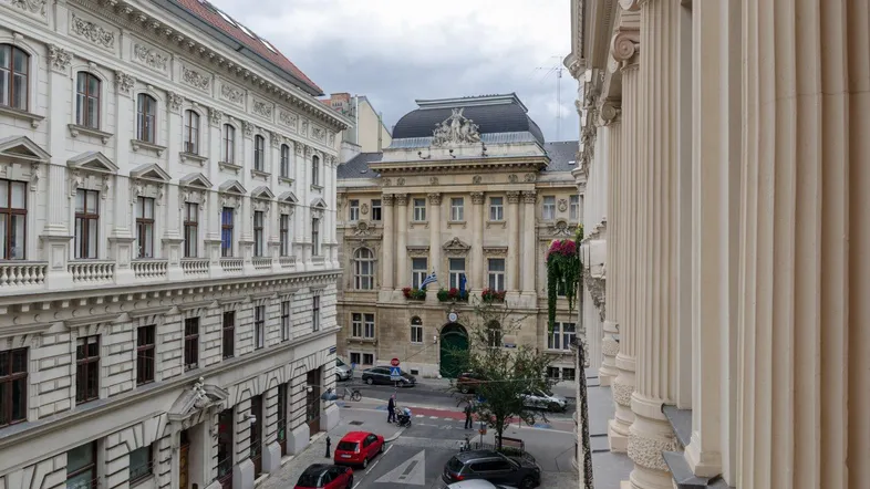 Blick von einem Balkon auf eine belebte Straße mit historischen Gebäuden und parkenden Autos.