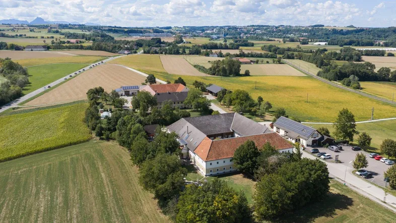 Luftaufnahme des weitläufigen Anwesens mit mehreren Gebäuden, umgeben von Feldern und grüner Landschaft.