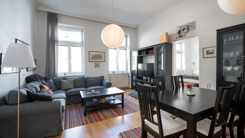 Geräumiger Wohn-Essbereich mit bequemer Couch, dunklem Esstisch und hellem Parkettboden.