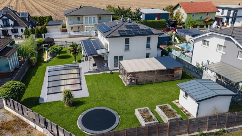 Luftaufnahme eines Einfamilienhauses mit großem Garten, Pool, Trampolin und Solaranlage auf dem Dach.