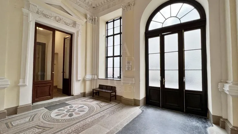 Großzügiger Eingangsbereich mit beeindruckender Stuckdecke, Mosaikboden und hohen Fenstern in einem Altbau.