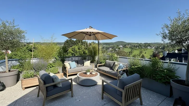 Geräumige Dachterrasse mit bequemen Loungemöbeln, Sonnenschirm und weitem Blick ins Grüne.