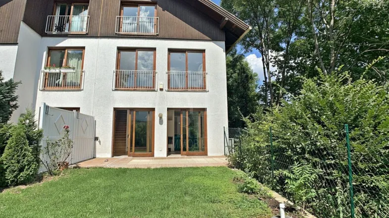 Weißes Reihenhaus mit Holzfassade, Balkonen und direktem Zugang zum grünen Gartenbereich.