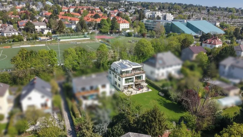 Luftaufnahme eines modernen Hauses mit Solaranlagen auf dem Dach und großem Garten in grüner Umgebung.