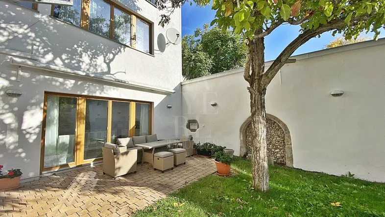 Möblierte Terrasse mit gepflastertem Bereich, Rasenfläche und einem Baum im Garten.