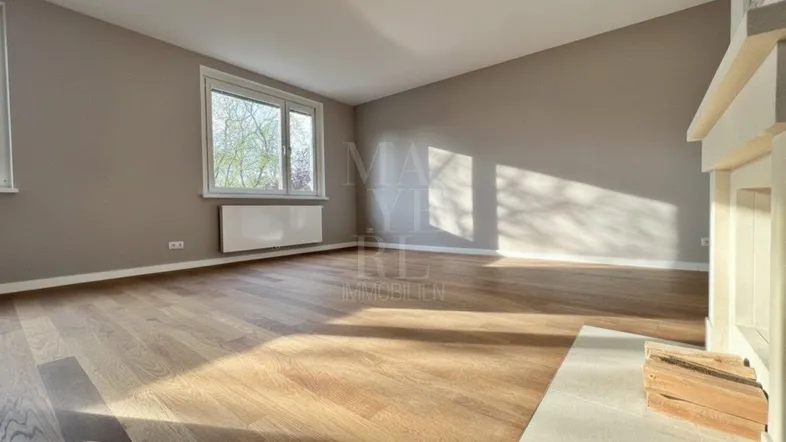 Heller Wohnraum mit Parkettboden und einem großen Fenster, das viel Tageslicht hereinlässt.