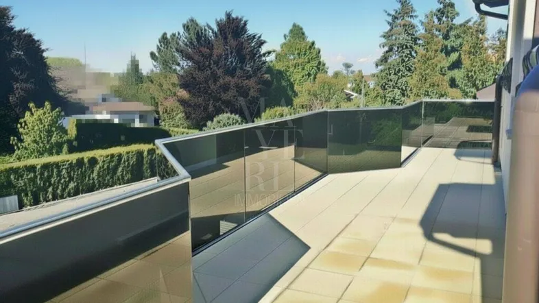 Sonnige Terrasse mit modernen Glasgeländern und weitem Blick ins Grüne und auf die Umgebung.