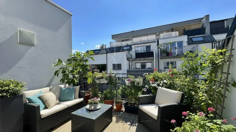 Möblierte Terrasse mit Pflanzen und Blick auf die umliegenden Gebäude unter blauem Himmel.