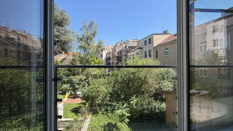 Blick aus dem Fenster auf einen grünen Innenhof mit Bäumen und umliegenden Gebäuden.