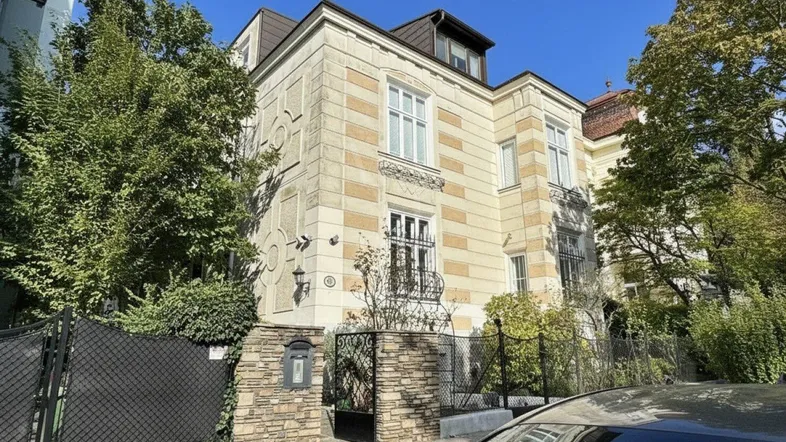 Elegantes Mehrfamilienhaus mit klassischer Fassade und schmiedeeisernem Zaun an einem sonnigen Tag.