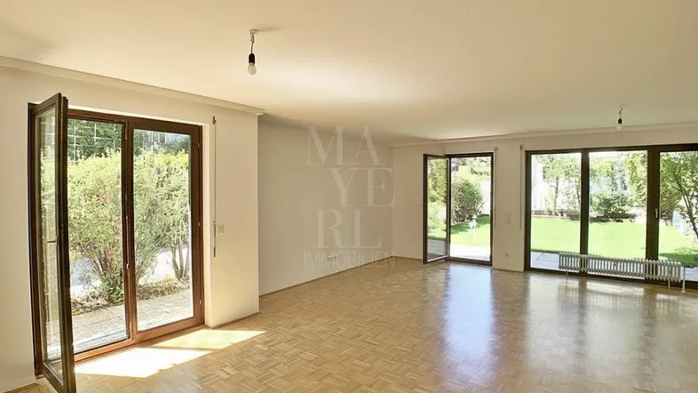 Helles und geräumiges Wohnzimmer mit Parkettboden und direktem Zugang zum Garten durch große Fenster.