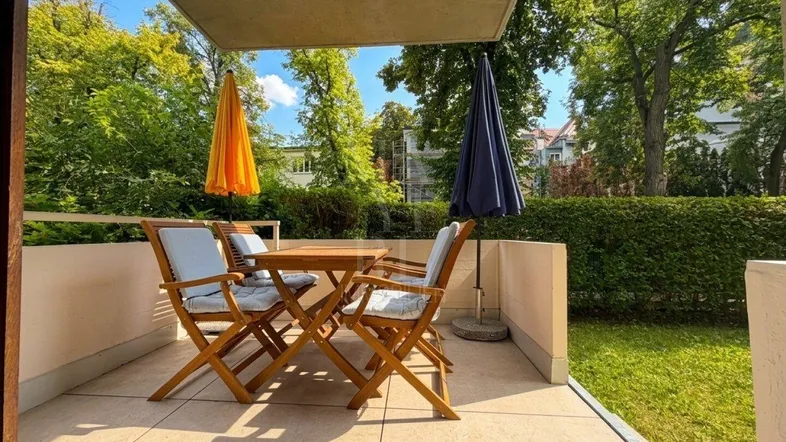 Möblierte Terrasse mit Sitzgelegenheiten und Sonnenschirmen, umgeben von grünen Bäumen.