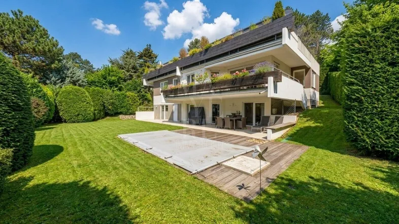Großzügiger Gartenbereich mit Rasenfläche, Poolabdeckung und einer Holzterrasse vor dem Haus.
