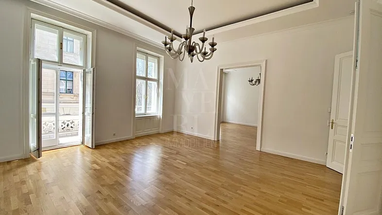 Helles Wohnzimmer mit hohen Decken, Parkettboden und Zugang zu einem französischen Balkon.