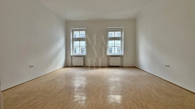 Helles, leeres Zimmer mit Parkettboden und zwei Fenstern, bereit zur individuellen Gestaltung.