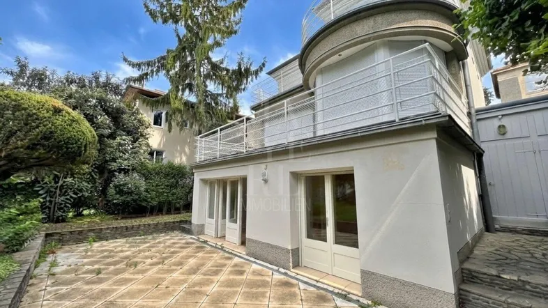 Außenansicht des Gebäudes mit einer gepflasterten Terrasse und Zugang zum Gartenbereich.