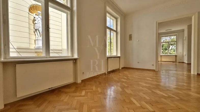 Helles Wohnzimmer mit Fischgrätparkett, hohen Decken und Blick auf eine historische Fassade.
