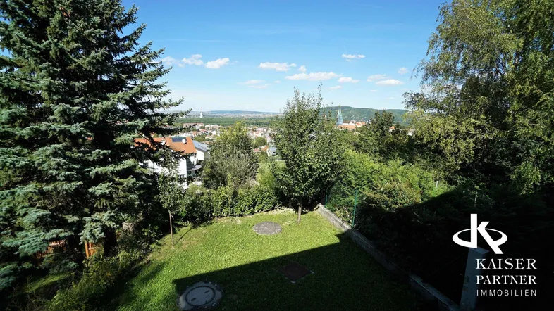 Grüner Gartenbereich mit Rasenfläche und weitem Blick über die Stadt und die umliegende Landschaft.