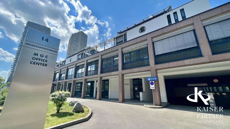 Moderne Bürogebäude-Fassade mit Beschilderung und Zufahrt zur Tiefgarage unter blauem Himmel.