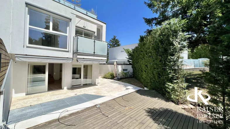 Moderne Hausfassade mit großen Fenstern, Balkon und einer geräumigen Terrasse im Erdgeschoss.