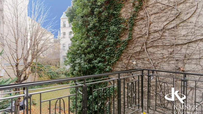 Kleiner Balkon mit schmiedeeisernem Geländer und Blick auf den begrünten Innenhof.