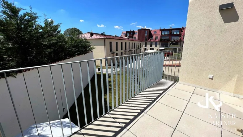 Heller Balkon mit Fliesenboden und Metallgeländer, bietet einen Blick auf die umliegenden Gebäude und Grünflächen.