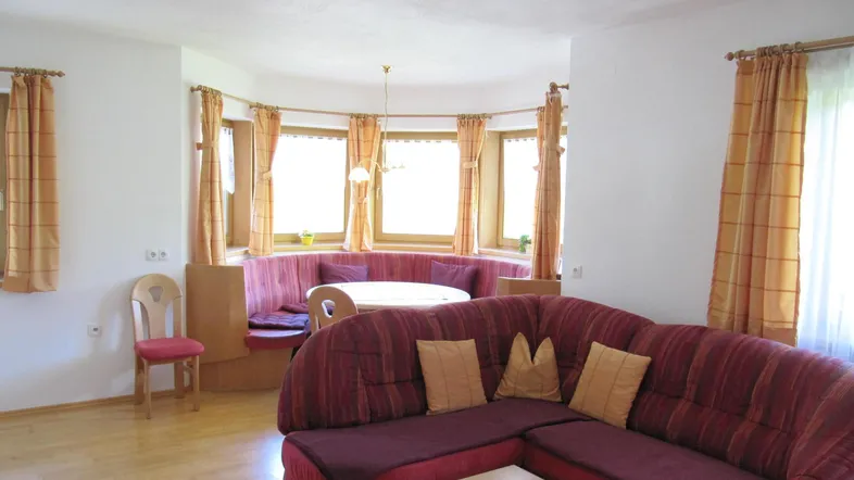 Gemütlicher Wohn-Essbereich mit rotem Sofa, hellem Holzboden und einer runden Essecke an den Fenstern.
