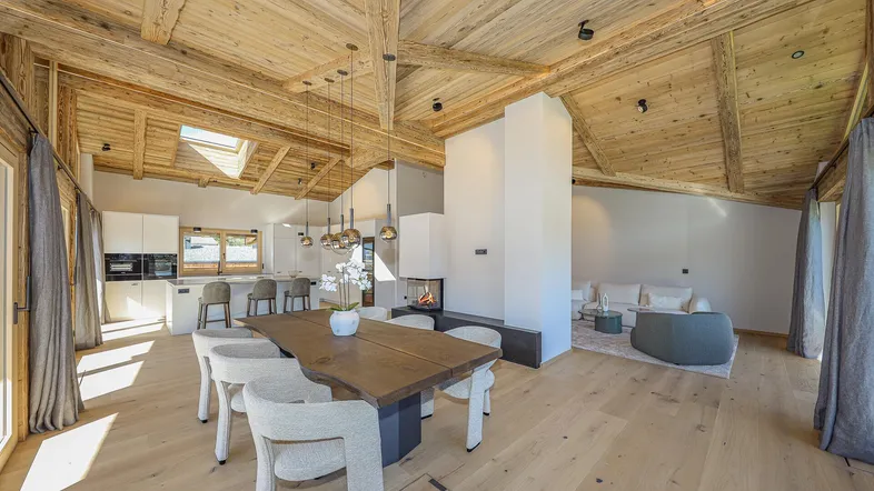 Geräumiger offener Wohn- und Essbereich mit Holzbalkendecke, Kamin und moderner Küche.