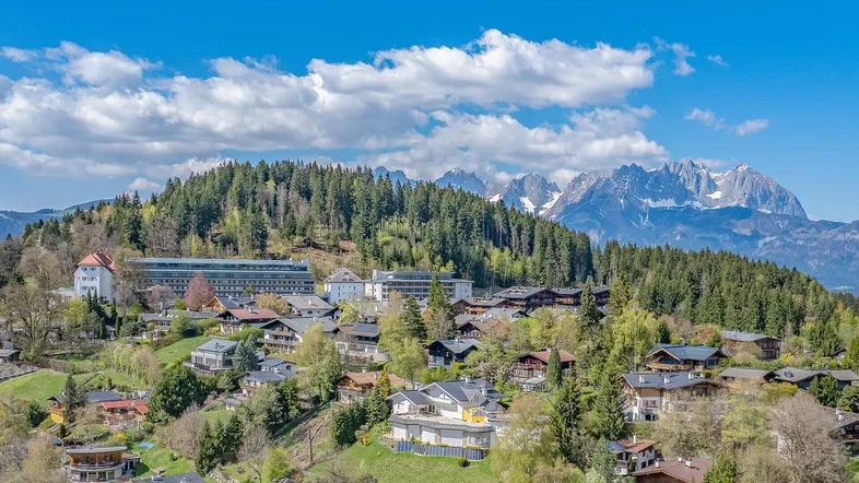 Panoramablick auf eine malerische Berglandschaft mit einem charmanten Dorf und schneebedeckten Gipfeln im Hintergrund.