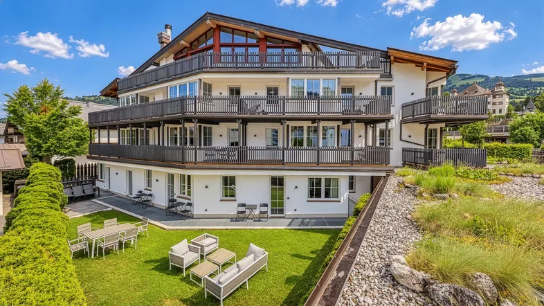 Modernes Apartmentgebäude mit mehreren Balkonen und einer gepflegten Gartenanlage mit Sitzgelegenheiten.