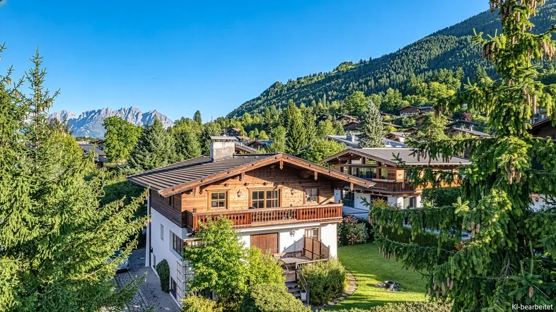 Traditionelles Holzchalet mit Bergblick und grüner Umgebung unter blauem Himmel.