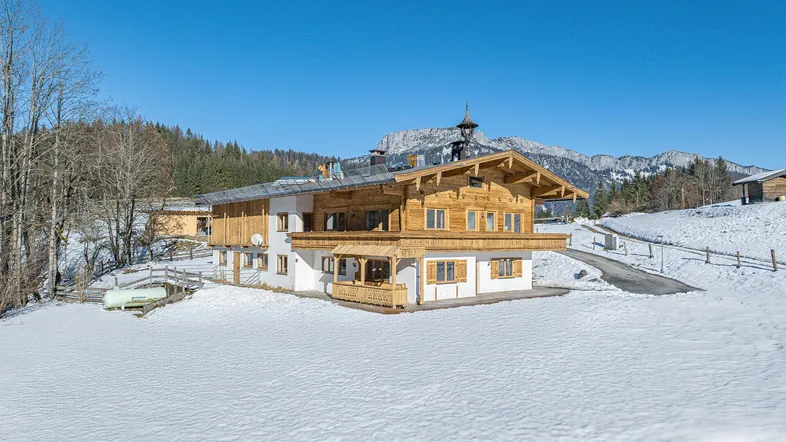 Traditionelles Chalet in verschneiter Berglandschaft unter strahlend blauem Himmel.