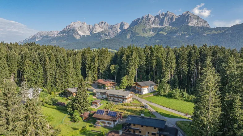 Panoramablick auf ein idyllisches Dorf umgeben von Wäldern und majestätischen Bergen.