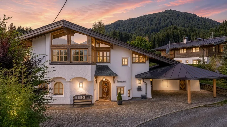 Charmantes Haus im alpinen Stil mit Carport und Bergblick bei Sonnenuntergang.