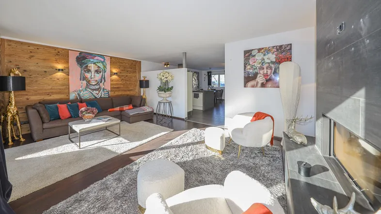 Geräumiges Wohnzimmer mit Holzwand, Kamin und modernen Kunstwerken, offen zum Essbereich.