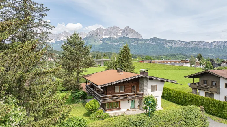 Traditionelles Chalet mit Holzelementen und Satteldach, umgeben von viel Grün und mit beeindruckendem Bergblick.