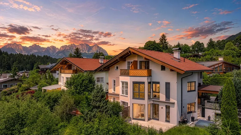 Beeindruckendes Haus mit traditioneller Architektur und atemberaubendem Bergblick bei Sonnenuntergang.