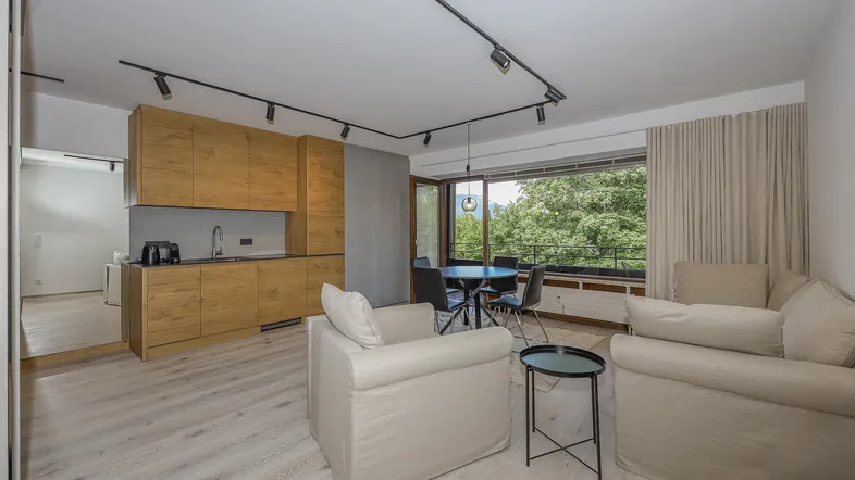 Helles, offenes Wohn-Esszimmer mit integrierter Küche und großem Fenster mit Blick ins Grüne.