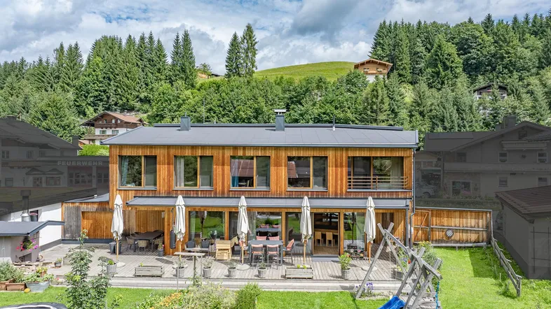 Modernes Holzhaus mit großer Terrasse, Essbereich im Freien und Blick auf die umliegende Natur.
