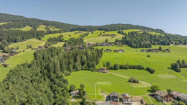 Luftaufnahme eines Grundstücks in einer idyllischen Berglandschaft mit umliegenden Häusern und viel Grün.