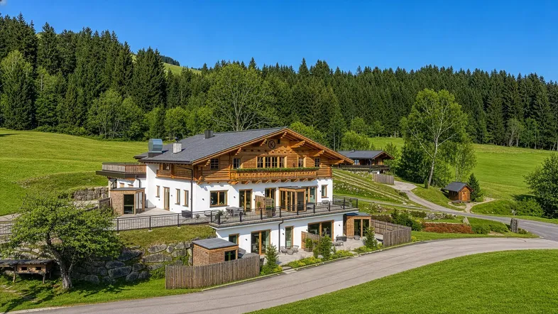 Großes Chalet im alpinen Stil mit Holzelementen, umgeben von grünen Wiesen und Wäldern.
