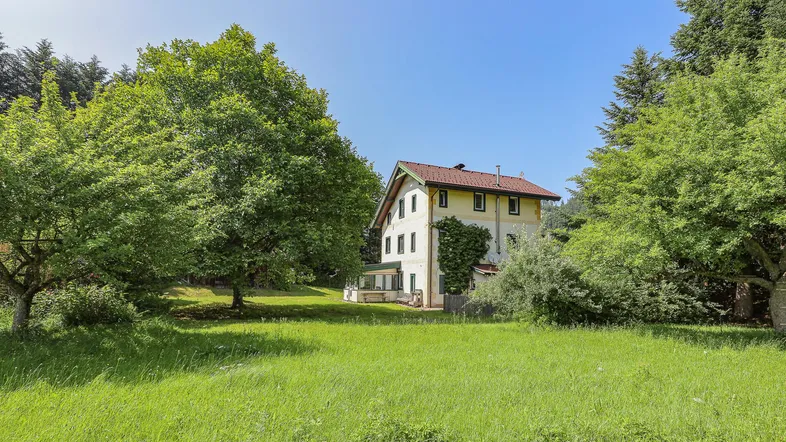 Traditionelles Landhaus umgeben von grünen Wiesen und Bäumen unter blauem Himmel.