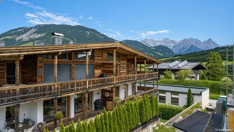 Traditionelles Holzhaus im alpinen Stil mit mehreren Balkonen und Bergblick unter blauem Himmel.