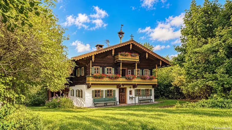 Traditionelles bayerisches Chalet mit Holzbalkonen und Blumenkästen, umgeben von grüner Natur.